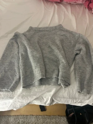 Grå stickad tröja från 157 - Mysig grå stickad tröja från 157 med rund halsringning och ribbade muddar vid ärmslut och nederkant. Tröjan har en enkel och avslappnad passform, perfekt för lager på lager. Materialet känns mjukt och behagligt mot huden. Den är lite nopprig därav priset!