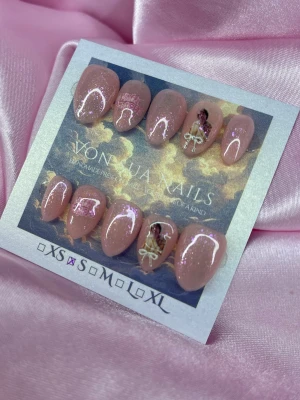 13 (S);Short Almond - Snygga press-on naglar i nude med glittrig finish, dekorerade med små motiv av änglar och rosetter. Naglarna har en oval form och är handgjorda. Perfekta för dig som vill ha en unik och trendig look.