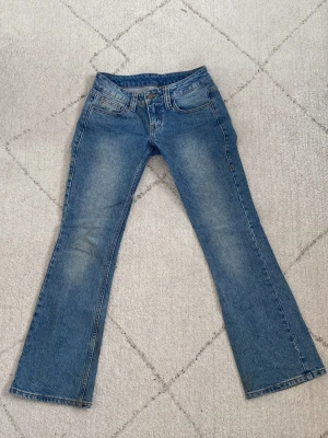 Lågmidjade bootcut jeans Brandy Melville - Ett par klassiska blå bootcut jeans med låg midja. Jeansen har fem fickor, bälteshällor och stängs med dragkedja och knapp. Tillverkade i denim med en snygg tvätt som ger en vintagekänsla. Midjemått: 37,5 cm tvärs över💕💕