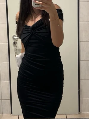 Svart klänning  - Snygg svart tight klänning med axelbandslös design och twistad detalj vid bysten. Lite längre än knäna på mig som är 170. Perfekt till mösspåtagning. 