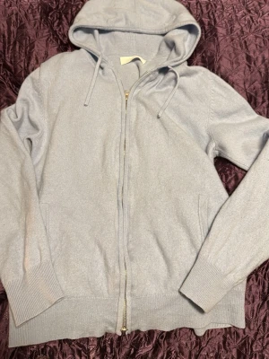 Kashmir hoodie - Ljusgrå hoodie med dragkedja framtill och två fickor. Tröjan har ribbade muddar vid ärmslut och nederkant samt justerbar huva med snören. Materialet ser mjukt och bekvämt ut, perfekt för en avslappnad stil. Lite liten på mig som är 170