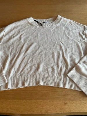 Beige cropped stickad tröja - Säljer en beige cropped stickad tröja med rund halsringning och långa ärmar. Tröjan har ribbade muddar vid ärmslut och nederkant, samt en avslappnad passform. Perfekt för lager på lager och enkel att styla till olika outfits.