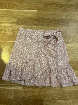 Blommig kjol från Shein  - Supersöt rosa kjol från Shein med vitt blommönster och volangkant. Kjolen har knytband i midjan och är perfekt för vår och sommar. 