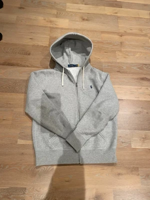 Grå zip hoodie från Polo Ralph Lauren - Snygg grå hoodie med dragkedja från Polo Ralph Lauren. Storlek S, en vag fläck vid fickan som syns på fjärde bilden, därav billigt pris. Hör av er vid frågor!