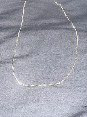Tunt silverfärgat kedjehalsband - Snyggt och enkelt halsband i silverfärg med tunn, fyrkantig kedja. Perfekt för dig som gillar minimalistisk stil och vill ha ett smycke som funkar till många olika looks. Halsbandet har ingen synlig logga eller  märke och är gjort i metall. 43cm lång. Frågor? Skriv gärna