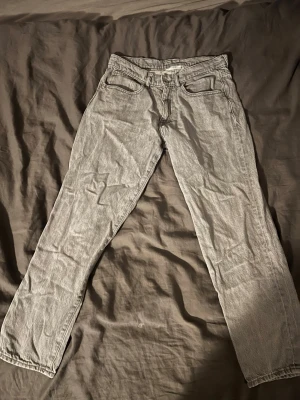Grå raka jeans i klassisk modell - Säljer ett par grå jeans med rak passform och fem klassiska fickor. Jeansen har normal midja och är tillverkade i denim. Perfekta för dig som gillar en enkel och stilren look.
