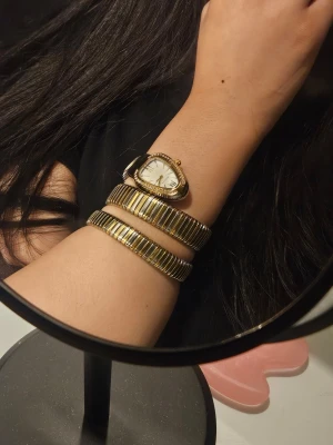 Guldfärgad ormformad klocka - Säljer en unik ormformad klocka i guldfärg med silverdetaljer. Klockan har ett vitt ur med guldmarkeringar och gnistrande stenar runt boetten. Armbandet är flexibelt och slingrar sig elegant runt handleden. Perfekt accessoar för dig som vill sticka ut. Behöver battaribyte