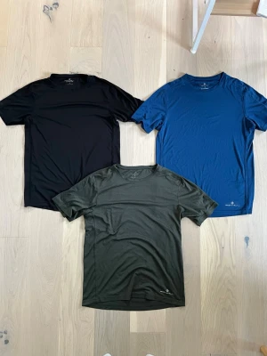 3-pack Ronhill tränings-t-shirts - Säljer tre snygga tränings-t-shirts från Ronhill i svart, blått och mörkgrönt. Alla har rund hals och är tillverkade i ett lätt och snabbtorkande syntetmaterial som passar perfekt för träning. Klassisk passform och kort ärm. Säljer då dem inte passa. Är som nya i skicket