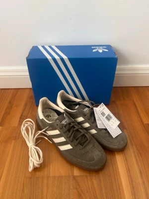 Adidas handball spezial - Säljer ett par Adidas handball spezial sneakers i olivgrönt mocka med klassiska vita stripes och gummisula. Skorna har lågt skaft och kommer med extra vita skosnören. Perfekt för dig som gillar retrostil och snygga detaljer.