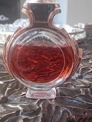 Elegant parfymflaska i glas olympea 50ml från början. - Säljer en elegant parfymflaska i klart glas med rundad form och vackra detaljer. Innehållet har en djup bärnstensfärgad ton som ger en lyxig känsla. Perfekt för dig som gillar snygga och klassiska doftflaskor att ha på hyllan. Från början 50 ml ,se bild