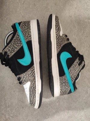 Nike SB Dunk Low Pro Elephant – åkta SB, bra skick i mocka, original box ingår - Säljer ett par Nike SB Dunk Low Pro “Elephant”, en klassisk SB-modell med elefantmönstrade paneler och turkos swoosh. Detta är en riktig SB Dunk, byggd för skate: tjock plös, Zoom Air-dämpning och slitstarka material. Modellen är populär både bland skatare och samlare.  Skorna är använda och åkta, vilket syns tydligt på yttersulorna (ojämnt slitage från skateboard). Ovandelen är i överraskande bra skick: mockan är fin, inga stora revor eller hål. Läderpaneler och elefantmönster är hela.