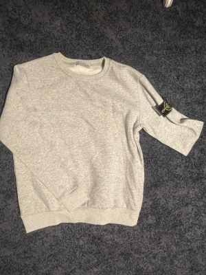  Stone Island sweatshirt, cp company  - Ljusgrå sweatshirt från Stone Island med klassisk rund halsringning och ribbade muddar. Tröjan har den ikoniska svarta logotypen med kompass på vänster ärm. Perfekt för en clean och avslappnad stil.