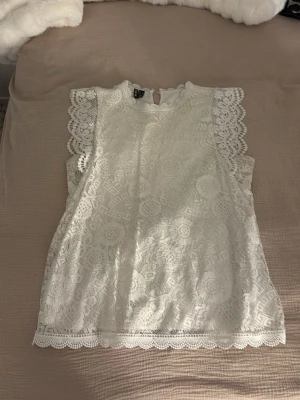 Vit spetsblus från Pieces - Superfin vit blus från Pieces med vackra spetsdetaljer och korta ärmar. Blusen har rund halsringning, knapp i nacken och dekorativa kanter. Perfekt att styla med jeans eller kjol för en söt look.