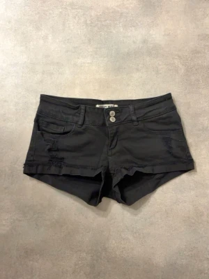 Svarta denimshorts från Only - Snygga svarta shorts från Only i denim med låg midja och slitna detaljer framtill. Klassisk femficksmodell med dubbla knappar och bälteshällor. Perfekta för varma dagar och enkel att matcha med olika toppar.