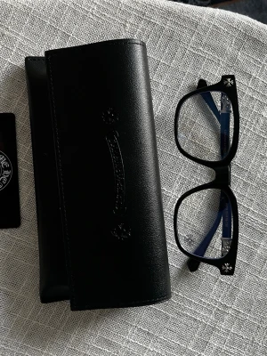 Svarta solglasögon från Chrome Hearts - Snygga svarta solglasögon från Chrome Hearts med fyrkantig form och silverfärgade detaljer vid gångjärnen. Bågarna är i blank svart acetat och har märkets ikoniska korsdetaljer på sidorna. Medföljer original svart fodral i skinn.