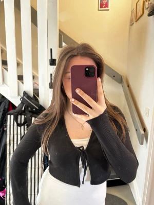 Svart ribbad cropped kofta med knyt - Trendig svart ribbad kofta i cropped modell med långa ärmar och knyt framtill. Perfekt att slänga över ett linne eller t-shirt för en snygg lager-på-lager-look. Mjuk och stretchig känsla, passar till det mesta i garderoben.