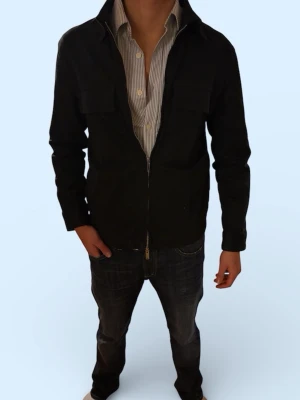 Svart overshirt med dragkedja - Stilren svart overshirt med dragkedja framtill och två bröstfickor. Jackan har klassisk krage och lång ärm, perfekt att bära över en skjorta för en avslappnad men snygg look. Tillverkad i ett mjukt bomullsmaterial.