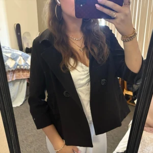 Svart trekvartsärmad kappa  - Jätte snygg trekvartsärmad kappa med rosetter vid fickorna och en rosett på ryggen. 💕