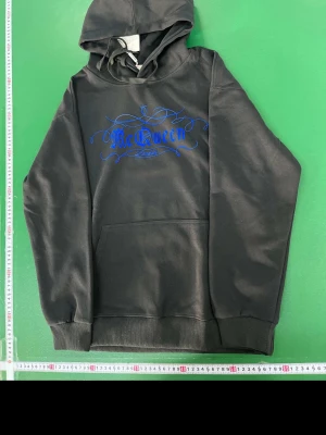 Svart hoodie från McQueen - Svart hoodie från McQueen med blått tryck framtill i snygg, snirklig stil. Klassisk känguruficka och ribbade muddar vid ärmar och nederkant. Tillverkad i mjukt material och har en stor huva för extra komfort.
