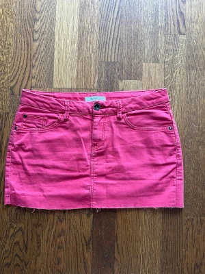 Rosa jeanskjol från Esprit - Kort rosa jeanskjol från Esprit med fem fickor, bälteshällor och rå kant nedtill. Kjolen har knapp och dragkedja framtill samt dekorativa sömmar på bakfickorna. Perfekt för dig som vill ha en färgstark och enkel kjol till sommaren. Skriv för fler bilder!