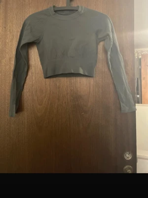Mörkgrön croppad långärmad topp - Snygg mörkgrön croppad topp med långa ärmar och rund hals. Tillverkad i ett stretchigt ribbat material som sitter tajt och bekvämt. Perfekt till träning