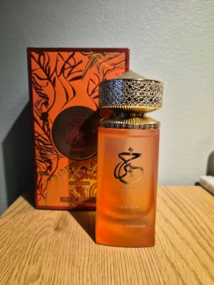 Paris Corner Fusion parfym - Exklusiv parfym från Paris Corner, Kfaar Fusion, i en frostad orange flaska med gulddetaljer och elegant mönstrad guldkork. Förpackningen är orange med guld och svarta detaljer och har ett lyxigt, orientaliskt uttryck.