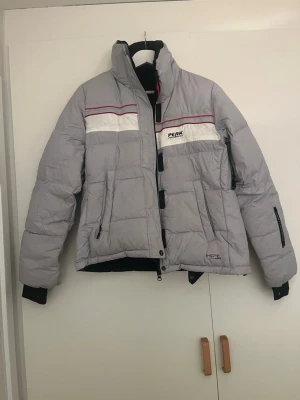 Peak Performance vinterjacka – dunjacka – storlek M - Snygg och varm vinterjacka från Peak Performance i klassisk design. Jackan är ljusgrå med röda och vita detaljer samt Peak Performance-logga på bröstet. Vadderad/dunfodrad och perfekt för kalla vinterdagar. Modellen har huva, dragkedja framtill, praktiska fickor och en sportig passform. Passar lika bra till vardags som till skidresa eller friluftsliv. Storleken är medium. Den är i bra skick. Skicka bara meddelande ifall ni undrar något mer.