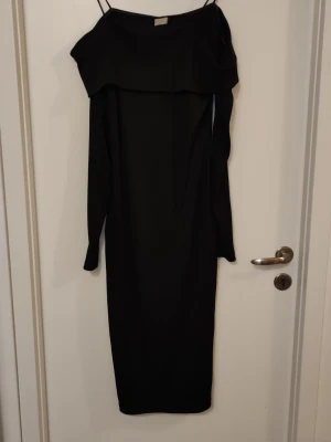 Svart offshoulder långklänning - Säljer en svart långklänning med offshoulder-design och långa ärmar. Klänningen har en stilren och enkel look med en bred kant upptill som ger en snygg detalj. Perfekt för dig som gillar minimalistisk stil.