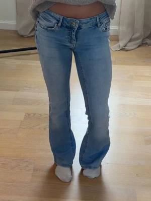 Ljusblå bootcut jeans med låg midja - Snygga ljusblå jeans med bootcut-modell och låg midja. Jeansen har klassiska fem fickor, dragkedja och knapp framtill. 