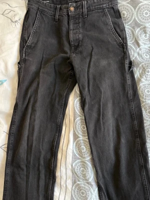 Svarta cargobyxor i denim Jack and Jones - Säljer ett par svarta cargobyxor i denim med raka ben och flera praktiska fickor på sidorna och bak. Byxorna har bälteshällor och knappgylf. Perfekta för en avslappnad streetwear-look.
