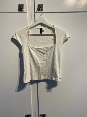 Vit croppad topp med fyrkantig ringning - Säljer en vit croppad topp från H&M med fyrkantig ringning och korta ärmar. Toppen är i mjuk bomull och har en slim passform som sitter snyggt på kroppen. 