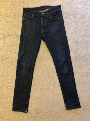 Mörkblå slim fit jeans från Nudie Jeans - Snygga mörkblå jeans från Nudie Jeans med klassiska fem fickor och kontrastsömmar. Jeansen har en slim passform och är tillverkade i stretchig denim för extra komfort. Bakfickorna har Nudie Jeans signaturbroderi. Nypris kostar dom 1600 kr och mitt pris är 500. Vid några frågor är det bara att höra av er !