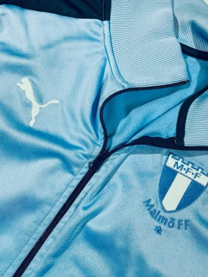 Ljusblå Malmö FF jacka från Puma - Ljusblå kofta från Puma / MFF.          logga på bröstet. Fin dragkedja, ribbad krage och detaljer i mörkblått. Materialet är mjukt och bekvämt, passar för både träning och matchdag.