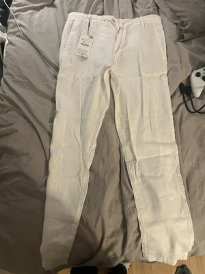 Vita linnebyxor från zara  - Snygga vita linnebyxor från Uniqlo med rak passform och klassisk midja. Byxorna har hällor för skärp och sidfickor, perfekta för en avslappnad och stilren look. Tillverkade i 100% linne för en luftig känsla.
