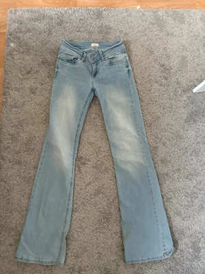 Nelly bootcut jeans - Ett par ljusblå bootcut jeans från Nelly med rosa broderi på bakfickorna. Några slitningar längst ner vid byxbenet där bak, men inget märkvärdigt. Nypris 699