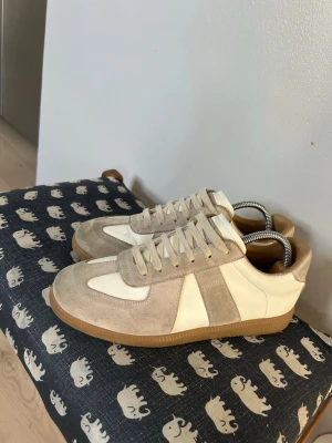 Maison margiela - Stilrena sneakers i beige mocka och vitt läder med klassisk gummisula. Skorna har lågt skaft, vita snören och en retroinspirerad design som passar till många outfits. Perfekta för dig som gillar minimalistisk och tidlös stil. Skorna är äkta 