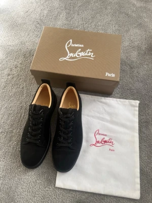 Svarta Christian Louboutin Sneakers - Svarta Louboutin sneakers med storlek 44. Med klassisk röd sula och svarta skosnören. Skorna är i nytt skick. Det finns ett litet ursprungligt fel med syet mellan skosulan. Diskutera med mig om ni vill ha ett prisförslag för det. Går inte att märka det.