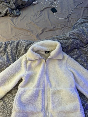 Vit teddyjacka från lager 157 - Supermysig vit teddyjacka från lager 157 med dragkedja framtill, två stora fickor och  krage. Jackan är fluffig och har en avslappnad passform, perfekt för kalla dagar. Materialet är mjukt teddytyg som håller dig varm och bekväm.