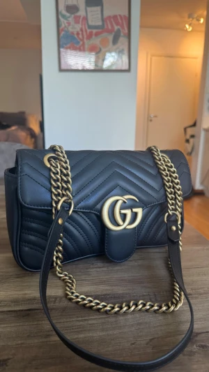 Svart Gucci Marmont handväska - Säljer en svart Gucci Marmont handväska i quiltat läder med guldfärgade kedjedetaljer och GG-logo framtill. Fick den 2019 & är använd sen dess. Säljer pga tröttnat på den. Har ej kvar förpackning pga flytt till ny stad🌸 har ej kvitto eller liknande 
