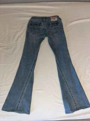 Blå bootcut jeans från True Religion - Snygga blå bootcut jeans från True Religion med klassiska kontrastsömmar och broderade bakfickor. Jeansen har låg midja och utsvängda ben, tillverkade i denim med lätt tvättad look. Perfekta för dig som gillar en avslappnad och trendig stil. Man kan diskutera pris💕