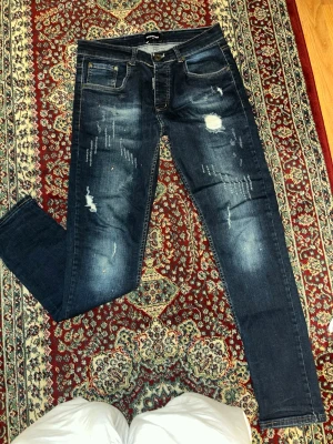 Mörkblå slitna jeans från Dsquared2 - Säljer ett par mörkblå skinny jeans från Dsquared2 med slitningar och distressed detaljer. Jeansen har klassisk femficksmodell, knappgylf och snygga slitna partier framtill för en trendig look. Perfekta för dig som gillar streetstyle och edgy mode.