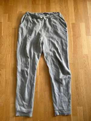 Grå mjukisbyxor från Polo Ralph Lauren - Snygga grå mjukisbyxor från Polo Ralph Lauren med dragsko i midjan och två sidofickor. Byxorna har en liten mörkblå logga broderad på vänster sida och är gjorda i mjukt bomullsmaterial. Perfekta för chill dagar eller när du vill vara bekväm. Storlek XL 18-20, skulle jämföra med en vuxen S