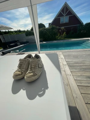 Vita sneakers från phillipe model - Säljer ett par klassiska vita sneakers från Veja med den ikoniska V-loggan på sidan. Skorna har en låg profil, vita snören och är tillverkade i läder med detaljer i grått. Perfekt för dig som gillar stilrena och trendiga skor. De är ganska så slitna pga hade de i regnet. Insidan av hälarna är också ganska slitna. Förutom allt de där så är skon i hyfsat bra skick 
