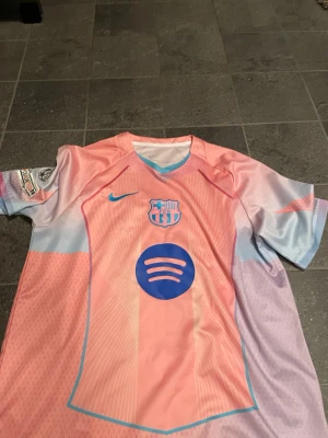 Barcelona matchtröja rosa/blå Nike - Säljer en Barcelona matchtröja i rosa och ljusblått med klubbmärke, Nike-logga och Spotify som sponsor på bröstet. RAPHINA #11 på ryggen. Tröjan har korta ärmar, UEFA Foundation-märke och Champions League-märke på ärmen. Tillverkad i lätt, ventilerande funktionsmaterial. 