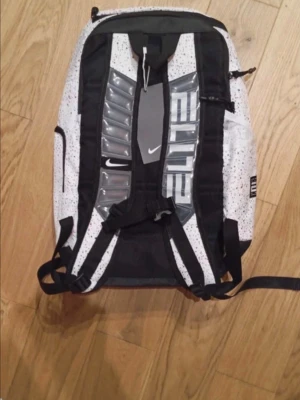 Nike Elite vit och svart ryggsäck - Nike Elite ryggsäck i vitt med svarta detaljer och färgstänk. Rymlig modell med vadderade axelband och tydlig ELITE-logga. Praktiska fack och slitstarkt material, perfekt för skola eller träning. Klassisk Nike Swoosh på både axelband och tag.