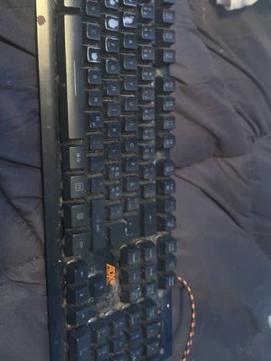 Svart tangentbord från ADX - Säljer ett svart tangentbord från ADX med orange logga och USB-kabel med orange-svart mönster. Tangentbordet har klassisk rektangulär form och svarta plasttangenter med vit text. Perfekt till gaming eller vardagsbruk vid datorn.