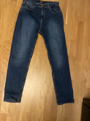 Mörkblå raka jeans från Lee - Säljer ett par klassiska mörkblå jeans från Lee med rak passform och fem fickor. Jeansen har en snygg tvättad look och är tillverkade i slitstarkt denimtyg. Perfekta för en avslappnad och stilren outfit. Storlek: 14-15 Y
