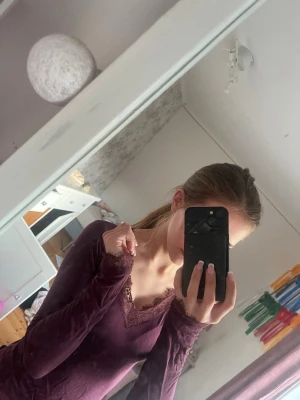 Vinröd långärmad topp från Gina Tricot - Vinröd långärmad topp från Gina Tricot med spetsdetaljer vid halsringningen och ärmsluten. Toppen har en v-ringad form och är i ett mjukt, stretchigt material som sitter snyggt på kroppen.