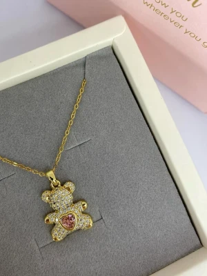 Guldigt halsband med nalleberlock - Supersött halsband med en guldig kedja och en gnistrande nalleberlock täckt av små klara stenar. Nallen har ett hjärta i rosa sten på magen som ger en extra gullig touch.                               Material: rostfritt stål Färg: Gult guld  Längd: 45-50cm  Ej använd utan kommer från min small business.Skicka ⭐ i meddelande för en hemlig rabatt.