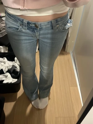 Ljusblå bootcut jeans från True Religion - Säljer ett par ljusblå bootcut jeans från True Religion med klassiska kontrastsömmar och snygga fickdetaljer bak. Jeansen har låg midja och är tillverkade i stretchigt denim för en bekväm passform. Köpt för ca 1200kr. Tyvärr så har en knapp åkt av, syns ej om man har mobilen där då jag brukar ha de. Lite slitet längst ner då dom e lite långa. Skriv vid ev frågor ❣️